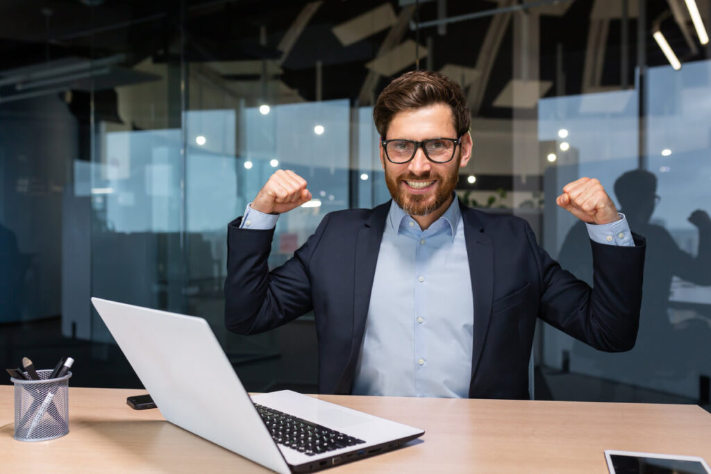 Mitarbeiter vor Laptop macht starke Pose mit den Armen